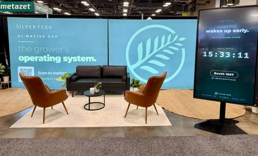 Silver Fern’s empty Cultivate booth, with a teal branded backdrop, lounge seating, plants, and a giant touchscreen.